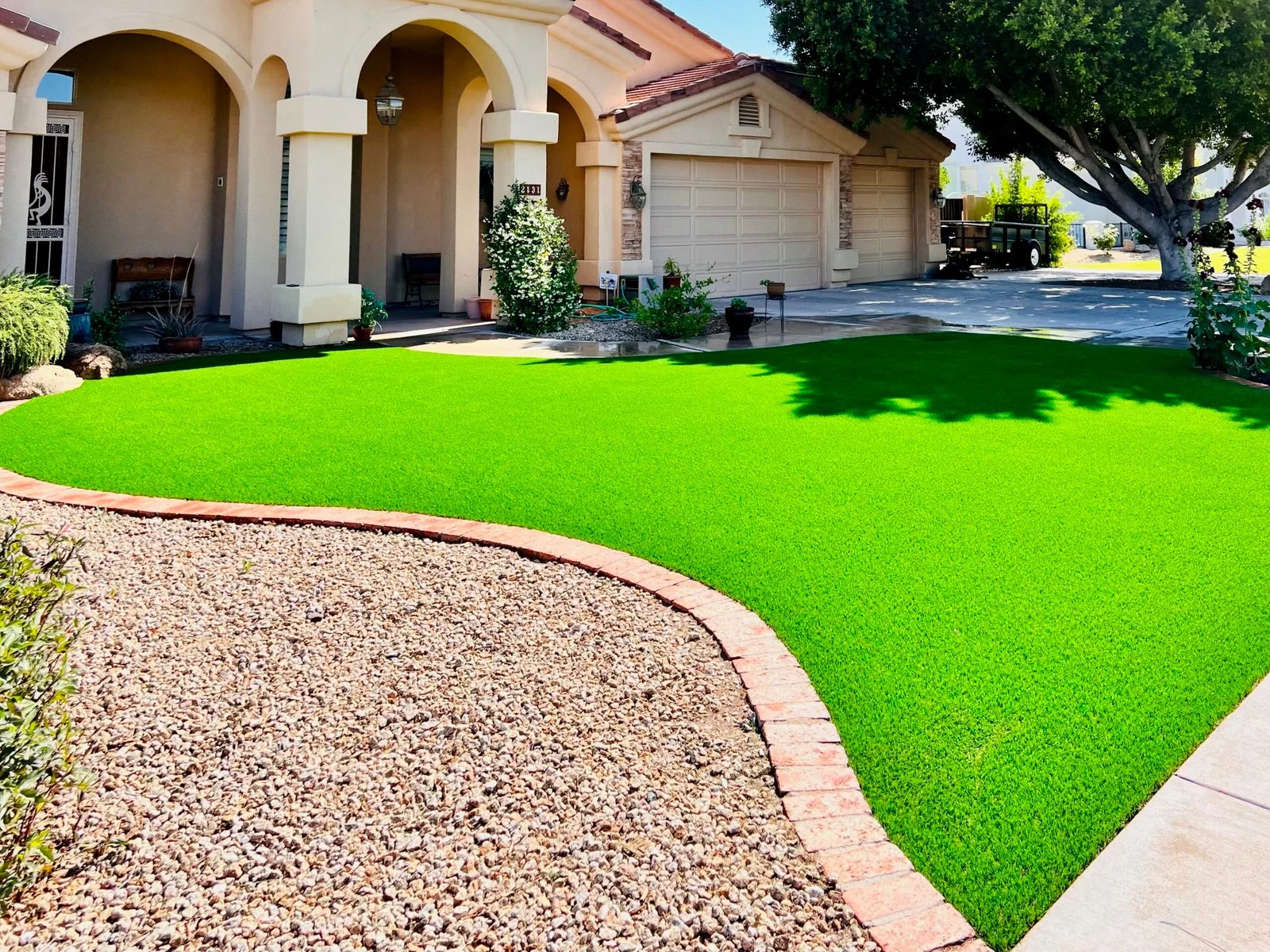 Artificial turf lawn installation in a residential front yard with decorative rock borders and mature landscaping.