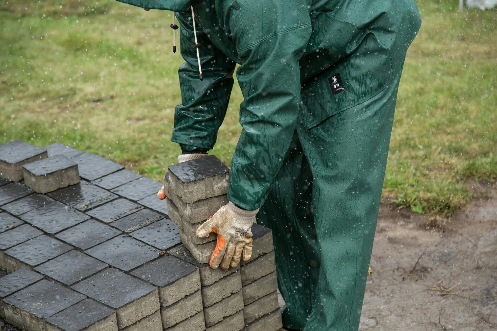 Hardscape installation with concrete pavers being laid in a rainy outdoor setting.