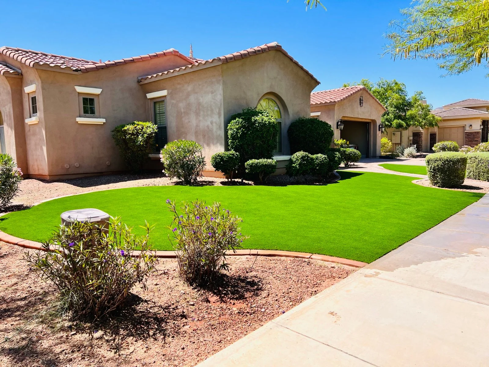Lawn care and landscape maintenance featuring a vibrant green lawn with manicured shrubs and desert plantings in front of a Southwest-style residential home.