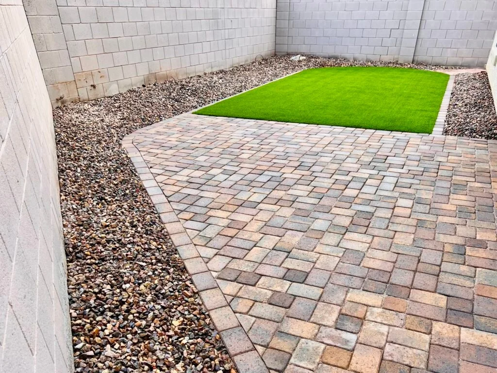 Sod installation and hardscape patio in a residential backyard with brick pavers, fresh turf, and decorative gravel borders.