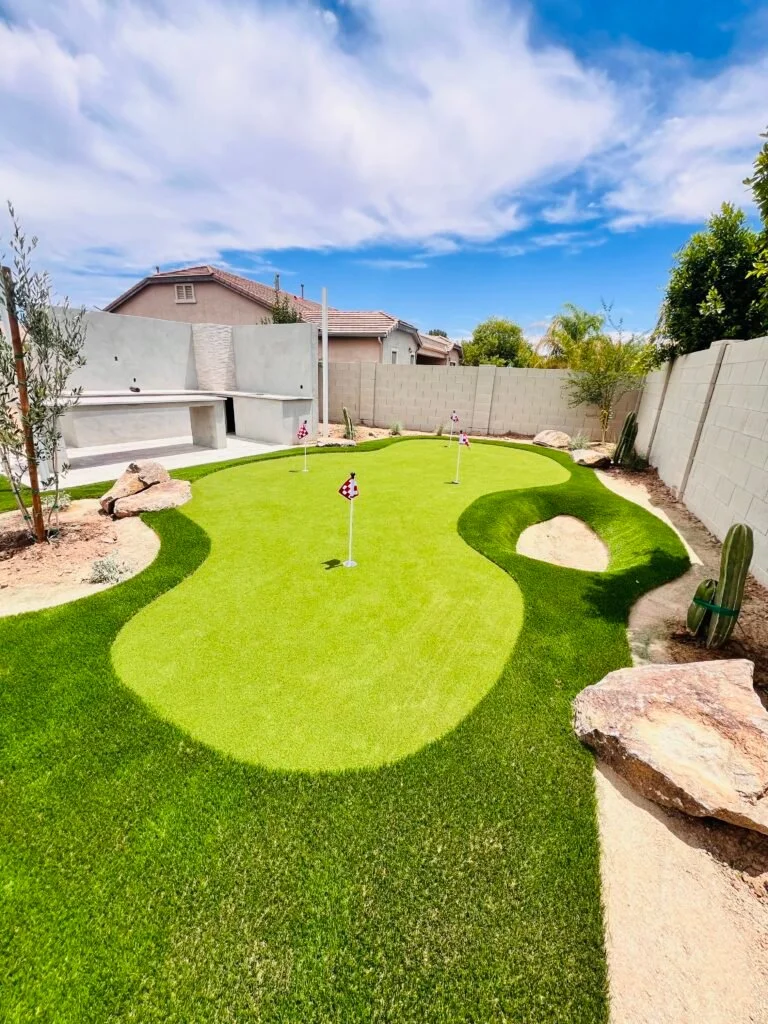 A sod-installed backyard with a custom putting green, sand bunkers, and decorative rock features in a residential landscape setting.