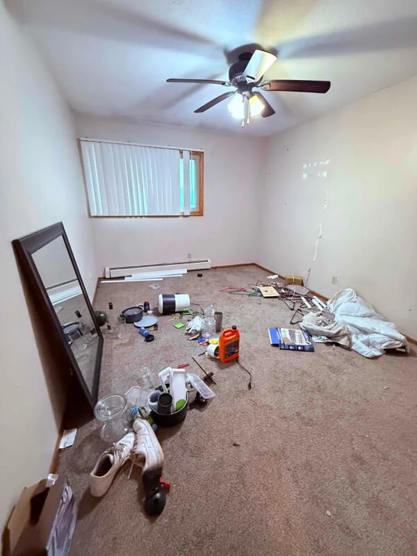 Before junk removal service showing an empty room cluttered with miscellaneous household items, construction materials, and debris scattered across the floor.