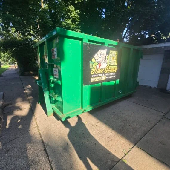 A bright green dumpster/junk removal container positioned on a residential sidewalk under trees.