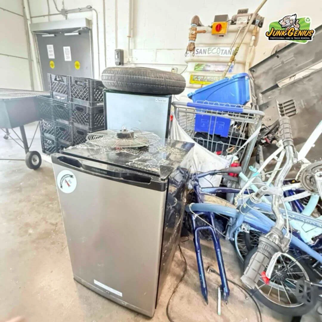 Collected junk items including appliances, bicycles, and miscellaneous debris in a warehouse workspace during a junk removal operation.