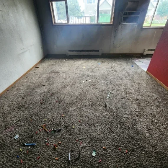 Floor debris removal service in progress in an empty residential room with windows and radiator.