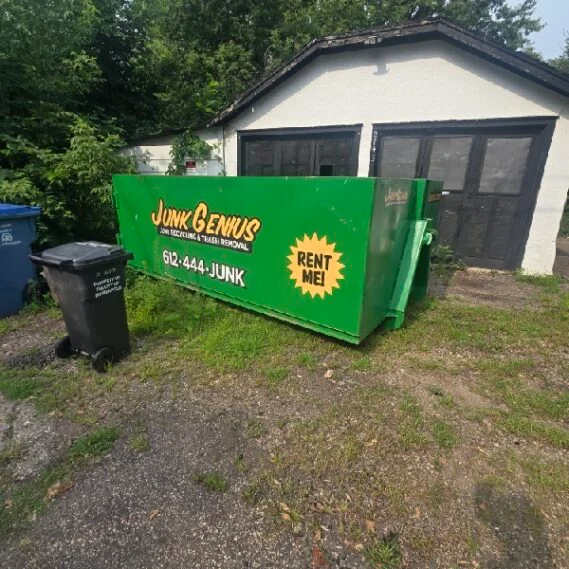 A green dumpster rental container from Junk Genius positioned in a residential driveway next to a garage.