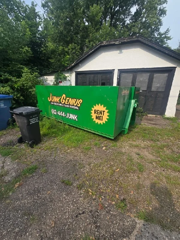 A green dumpster rental container from Junk Genius positioned in a residential driveway in front of a garage.