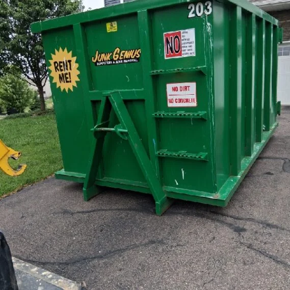 A green junk removal dumpster container numbered 203 positioned on an asphalt surface outdoors.