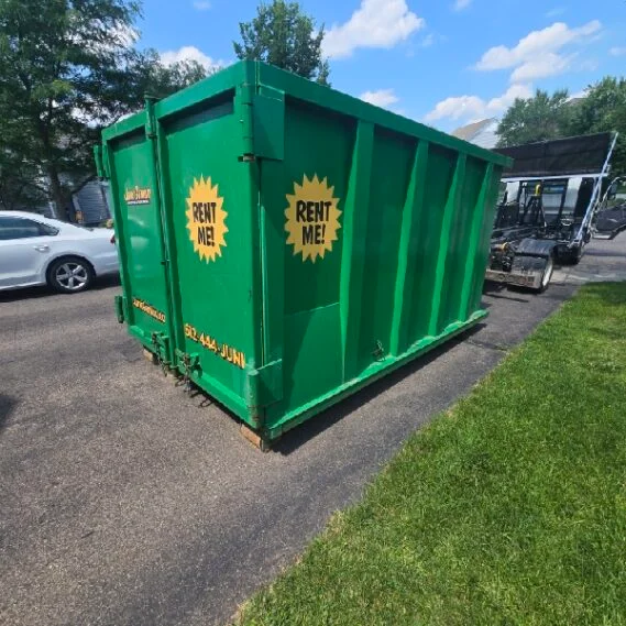 A green rental dumpster container displayed in an outdoor parking lot, showing the company's junk removal equipment available for rent.
