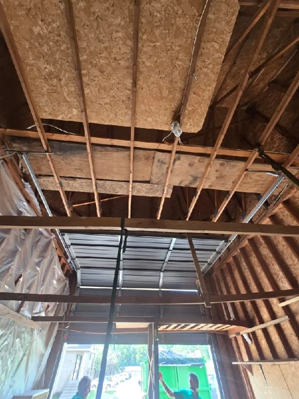 Interior demolition and junk removal work in progress, showing exposed framing, insulation removal, and structural gutting of a residential space.