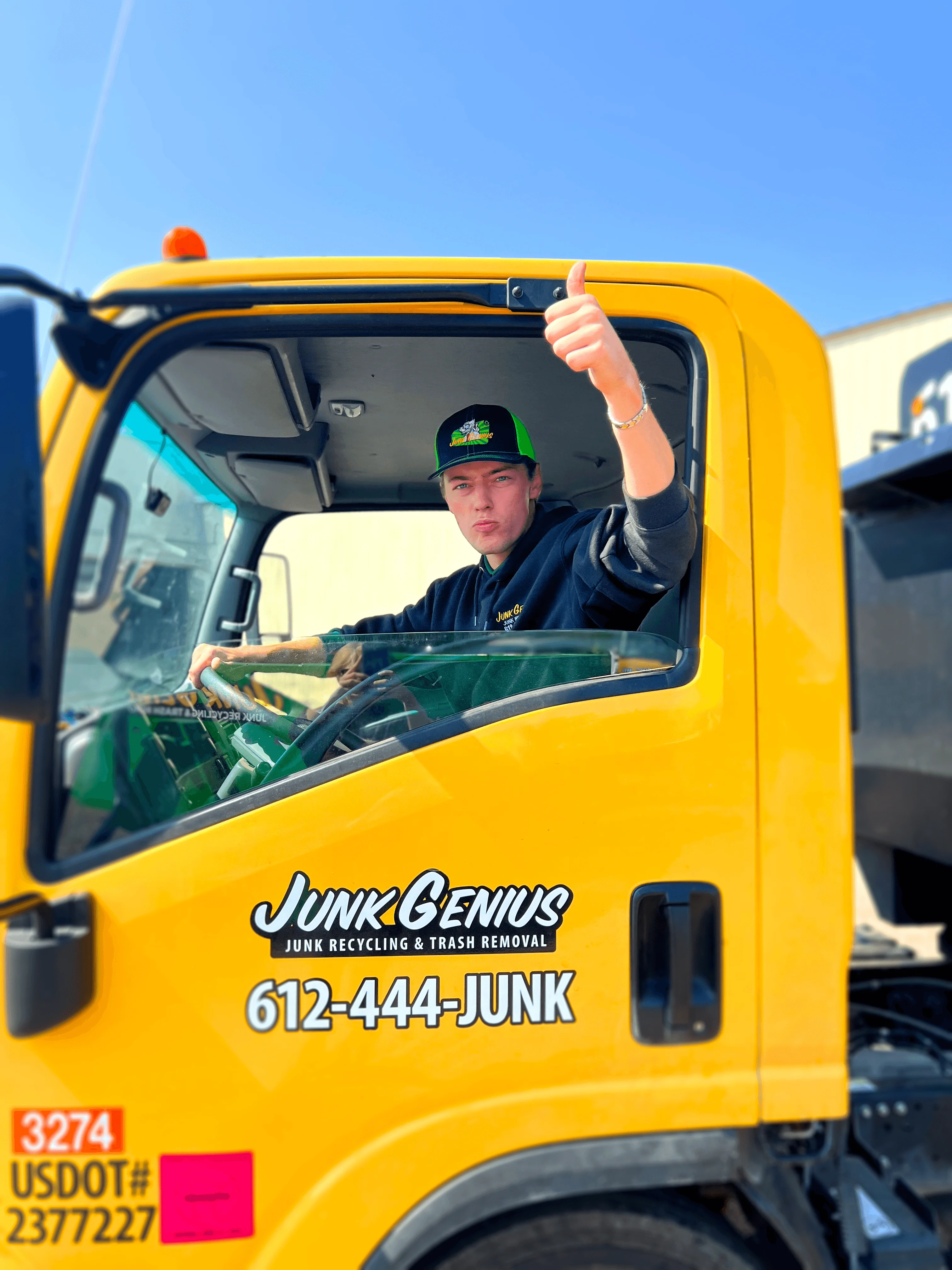 A Junk Genius junk removal truck with driver giving a thumbs up, representing the service and customer-facing brand experience.