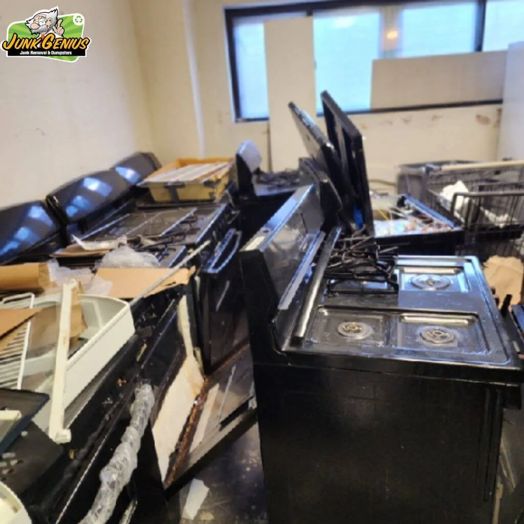 Junk removal and appliance disposal service in progress, showing a warehouse or storage facility filled with discarded appliances including stoves, refrigerators, and other large items ready for removal.