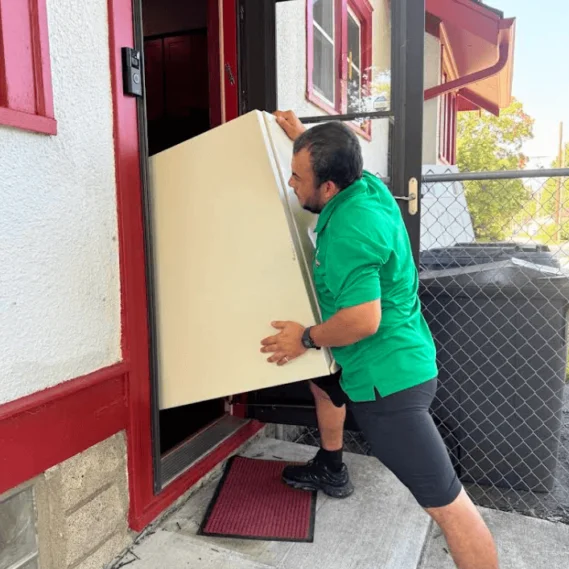 Junk removal service in progress as a worker carries a large panel or sheet material out of a residential building entrance.