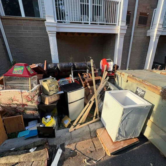 Junk removal service in progress in a residential courtyard, showing accumulated debris, appliances, wood materials, and miscellaneous items staged for removal.