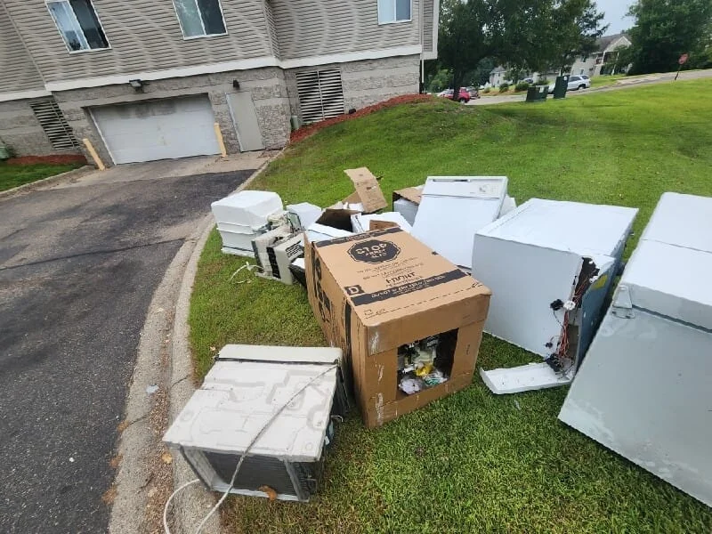 Junk removal service in progress on a residential front lawn, showing collected appliances, furniture, and miscellaneous debris staged for hauling.