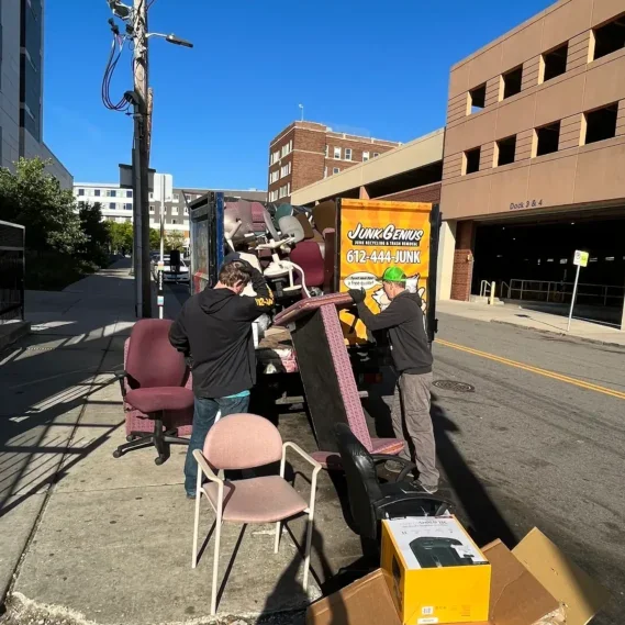 Junk removal service in progress on a city street, with workers loading furniture and household items onto a truck.