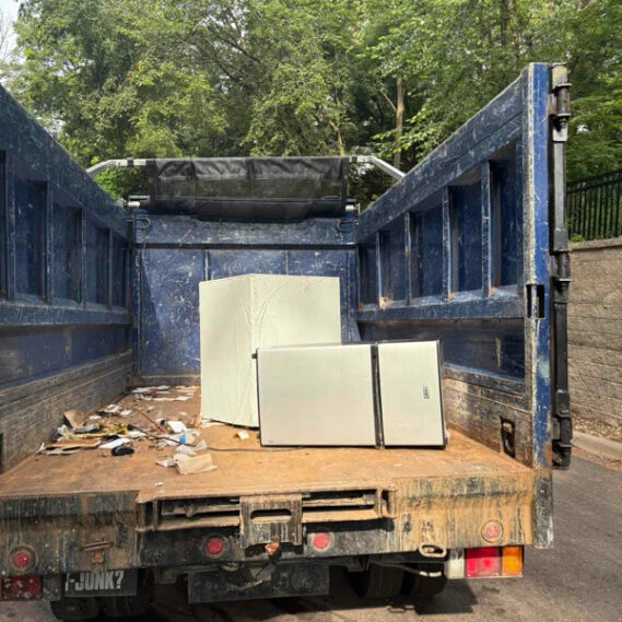 Junk removal service in progress showing appliances being loaded into the back of a worn blue commercial truck bed.