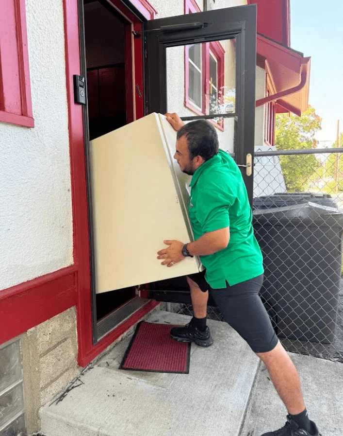 Junk removal service in progress showing a worker carrying a large sheet of drywall or similar material out through a residential doorway.