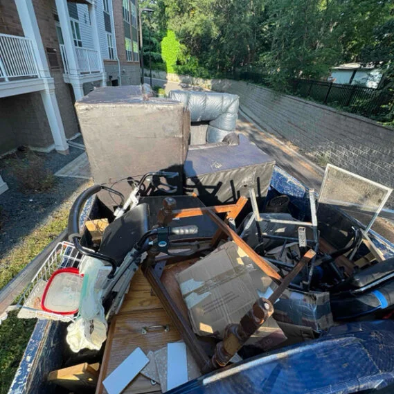 Junk removal service in progress, showing a truck bed filled with collected household waste, electronics, and furniture from a residential property.