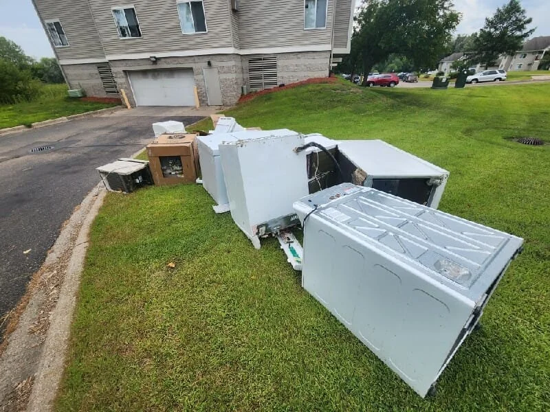 Junk removal service in progress showing discarded appliances and household items on a residential lawn.