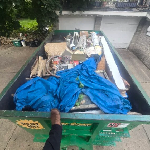 Junk removal service in progress showing a large green dumpster bin filled with miscellaneous household waste, debris, and discarded items during an active cleanup job.