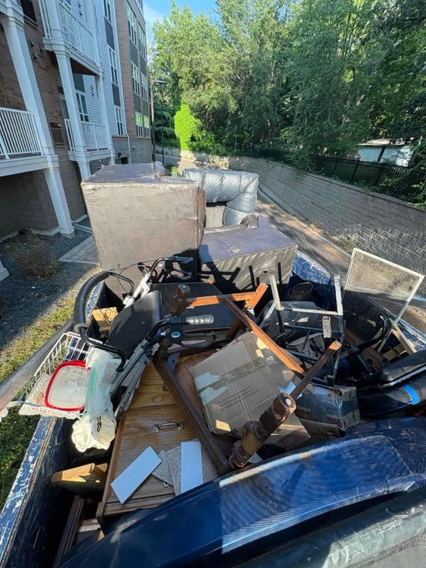 Junk removal service in progress, showing a truck bed filled with collected debris, appliances, and miscellaneous items from a residential property.