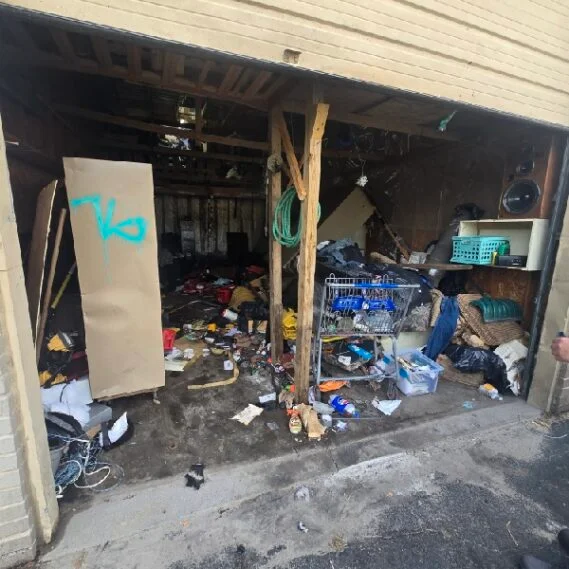 Junk removal service in progress showing a cluttered garage filled with accumulated debris, boxes, and miscellaneous items awaiting clearance.
