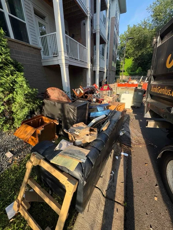 Junk removal service in progress showing loaded dumpster trucks and debris collection in an alleyway behind a residential building.