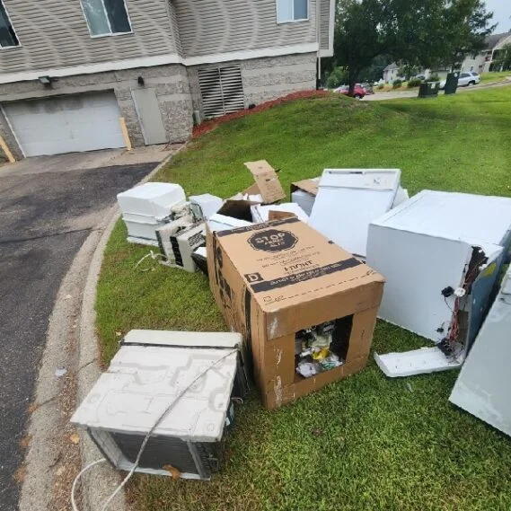 Junk removal service in progress showing collected appliances and household items on a residential front lawn.