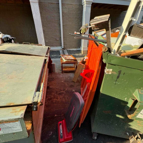 Junk removal service in progress showing a residential property with a loaded red waste container and various discarded items being sorted and collected.