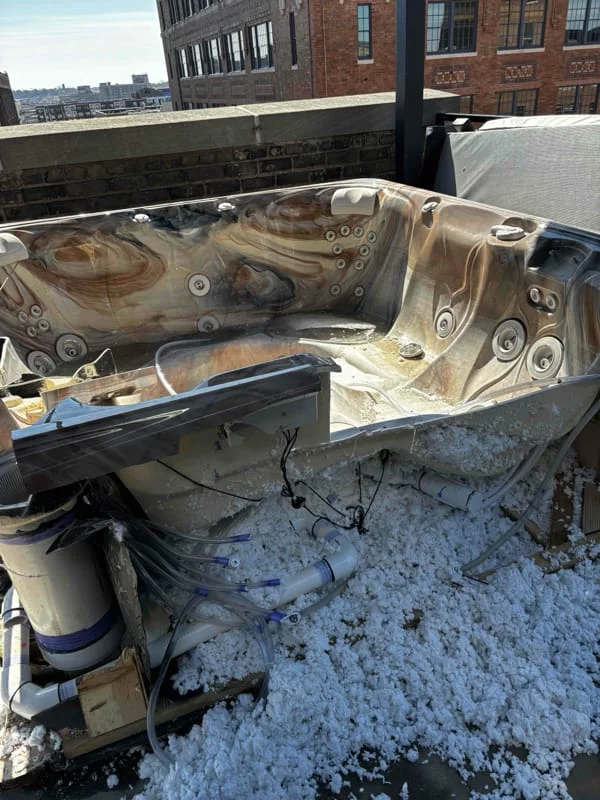 Junk removal service in progress showing a large hot tub being dismantled and removed from a rooftop in an urban setting.