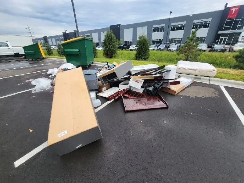 Junk removal service in progress showing a large pile of discarded furniture, appliances, and miscellaneous waste collected in a parking lot.