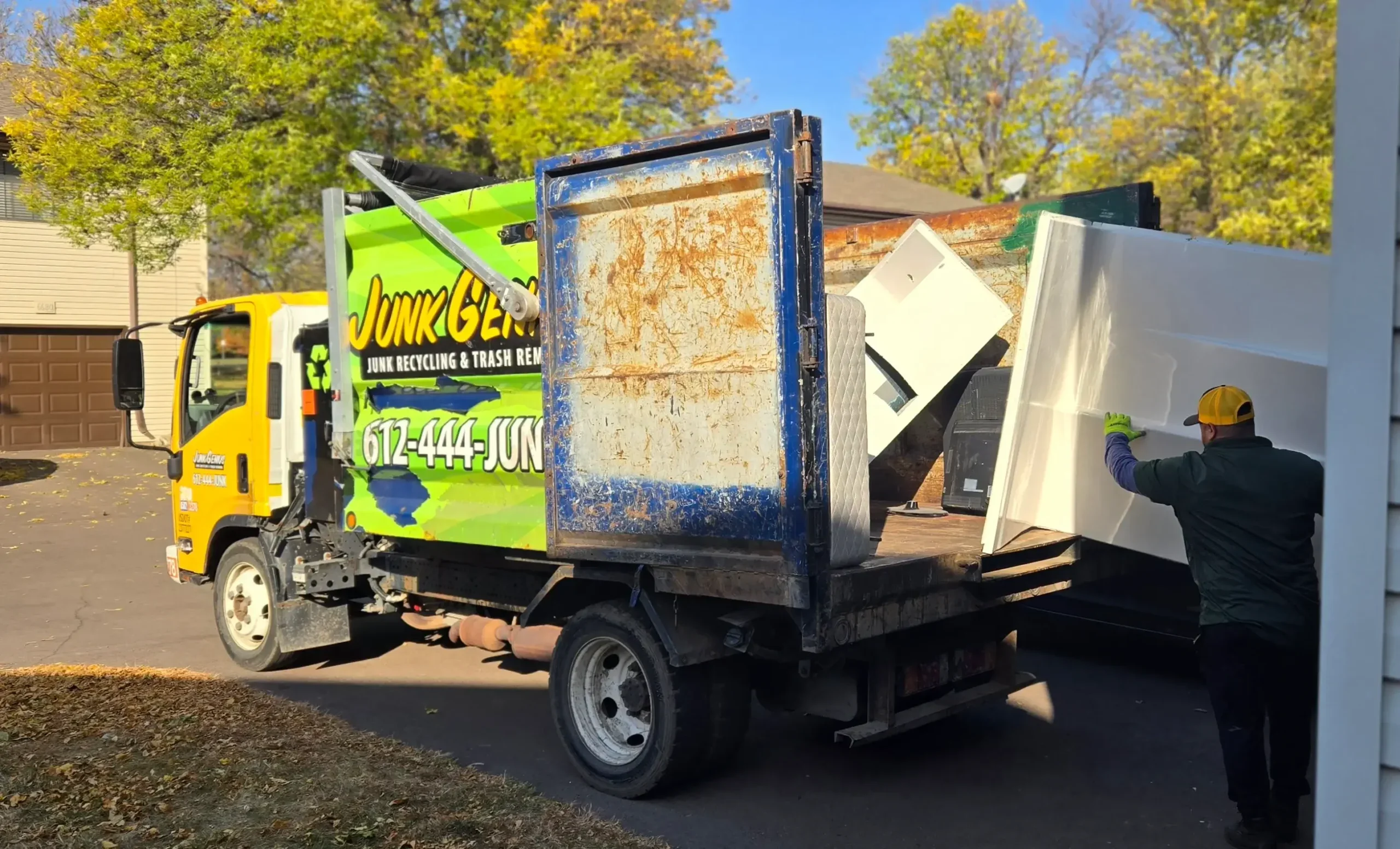 Junk removal service in progress, with a worker loading bulky items including doors and debris into a branded Junk Gee truck at a residential driveway.
