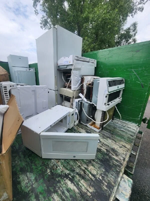 Junk removal service showing a collection of discarded appliances and household items in a waste disposal container.