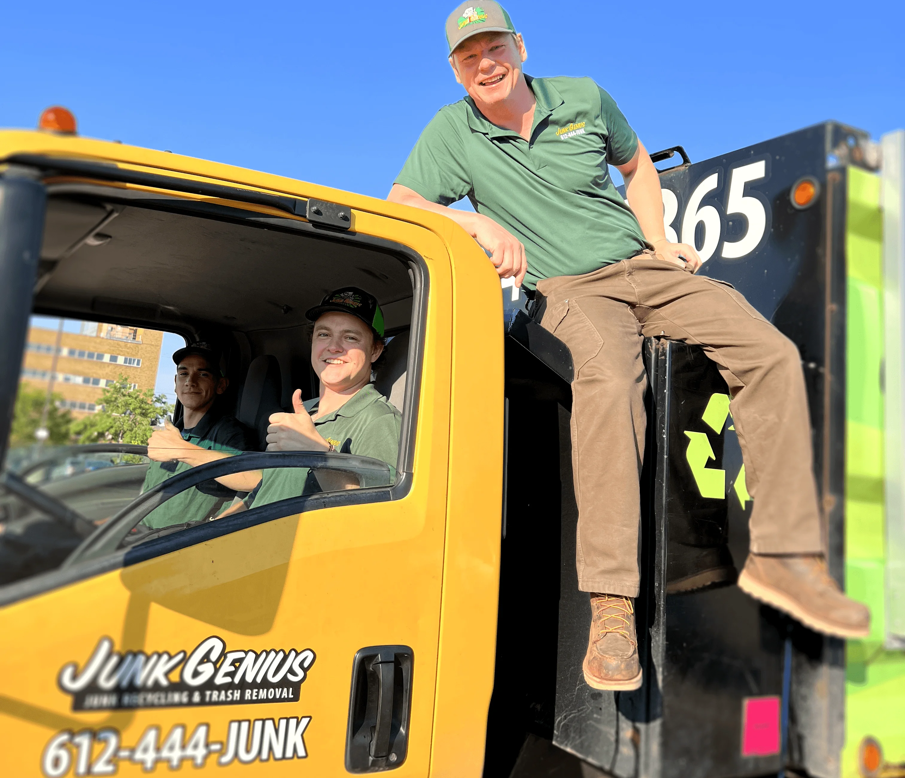 Junk removal service team posing with a yellow Junk Genius truck and attached trailer on a clear day.