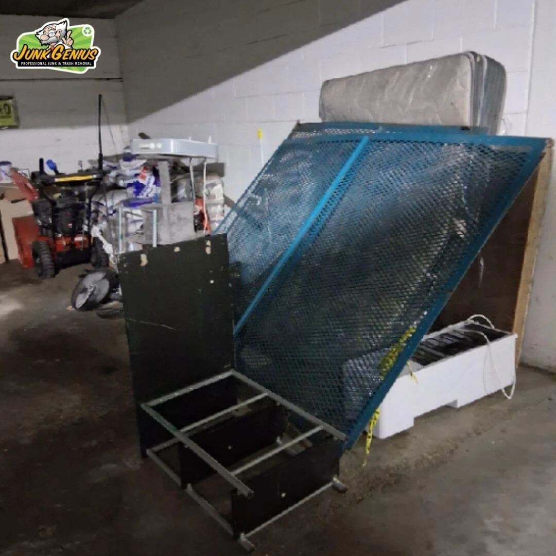Junk removal service-in-progress showing bulky items including a mattress, furniture, and other household goods secured with blue mesh netting on a transport vehicle in a warehouse facility.