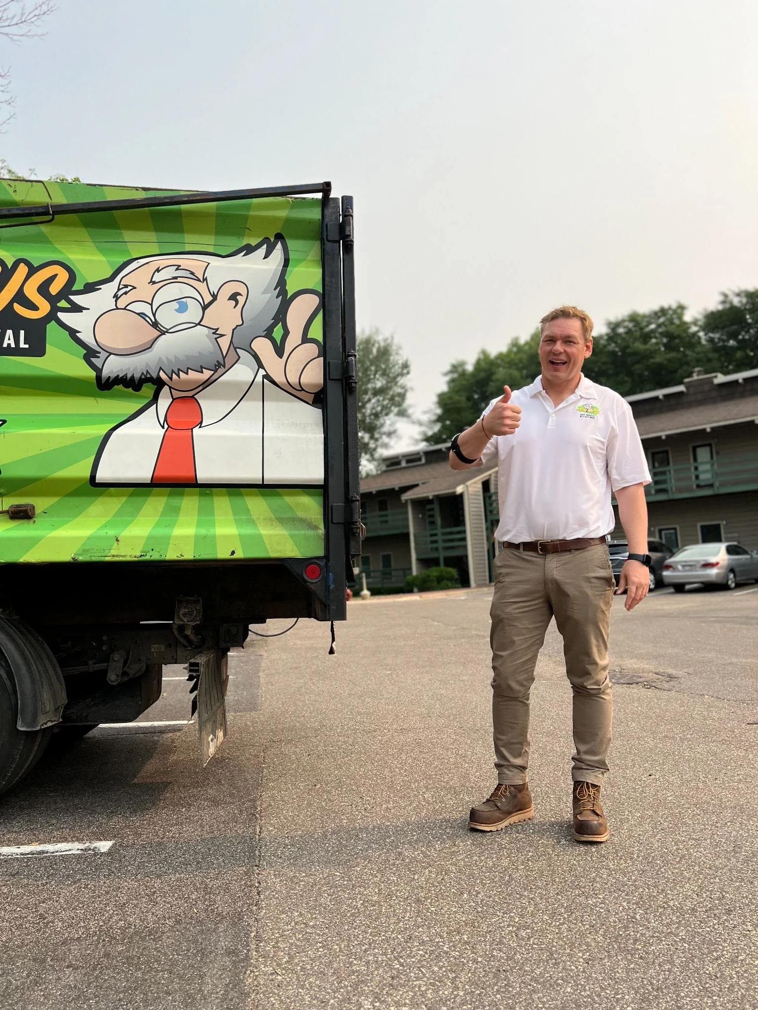 A junk removal truck with branded graphics featuring a cartoon mascot, parked in a residential driveway during a service call.