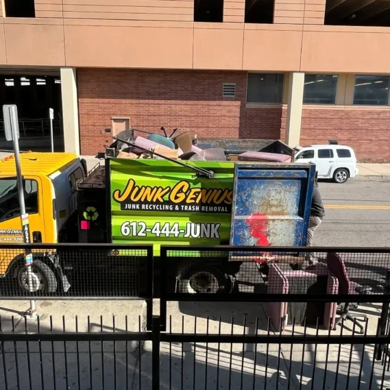 A junk removal truck with a full load of miscellaneous debris and items being transported for recycling and trash removal in an urban street setting.