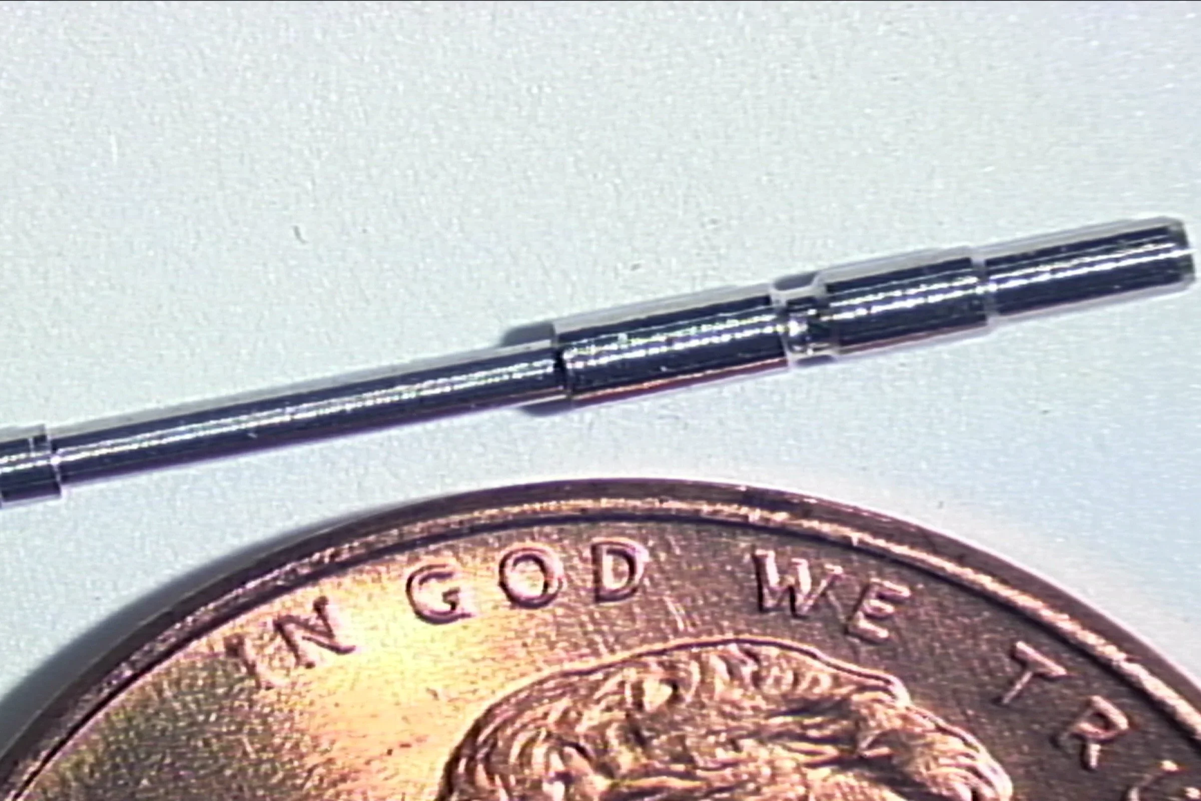 A ballpoint pen shown next to a British coin for scale comparison on a white background.