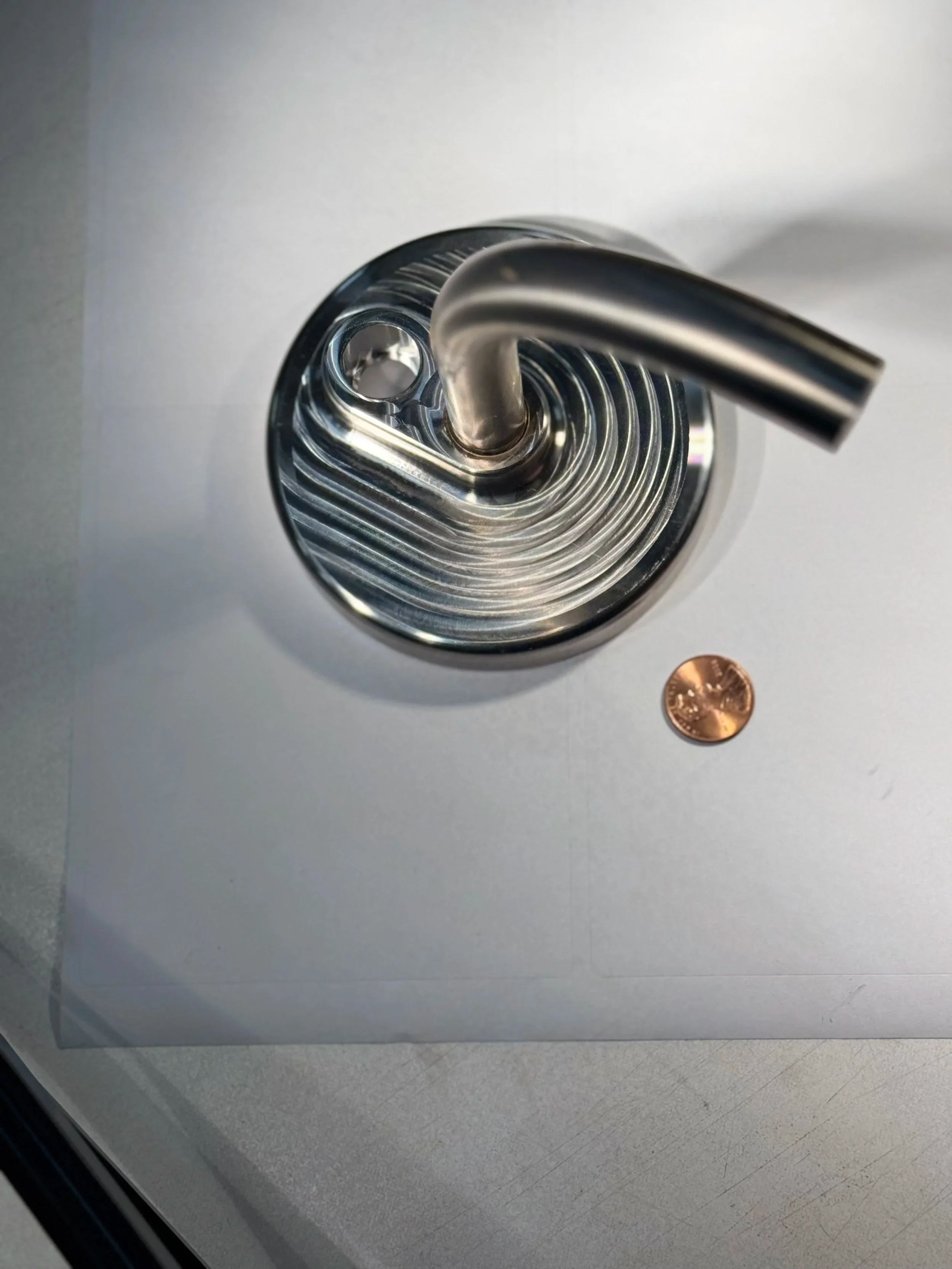 Decorative metal spiral coil next to a penny for scale on a white surface, showing product size reference.