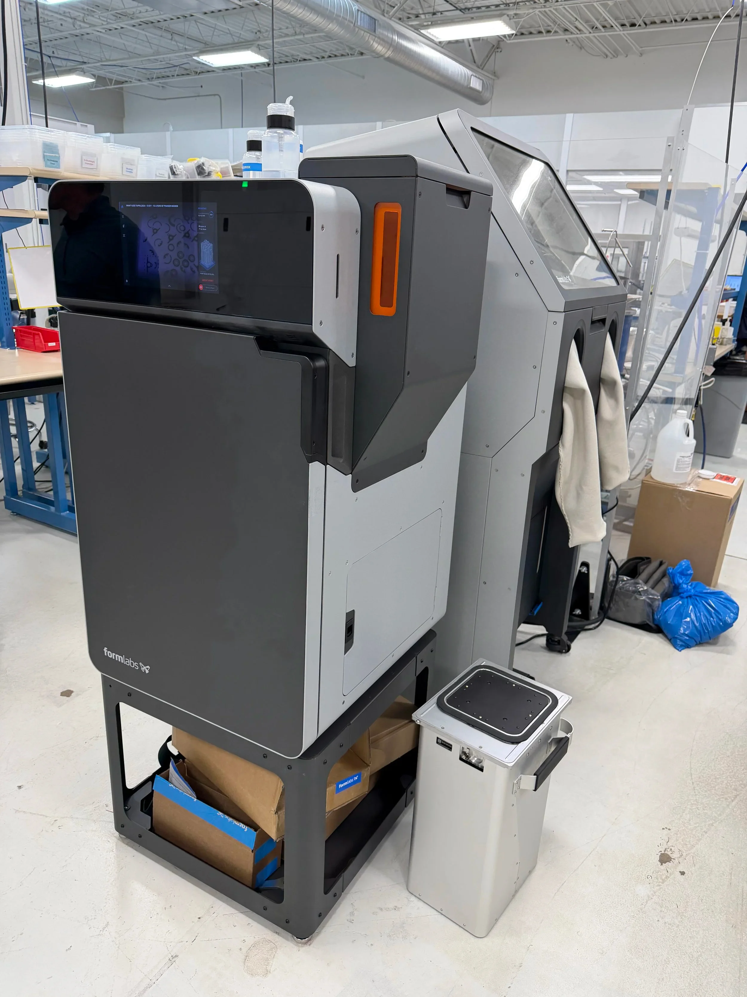 A Formlabs 3D printer displayed in a laboratory or manufacturing facility workspace with accompanying equipment and storage.