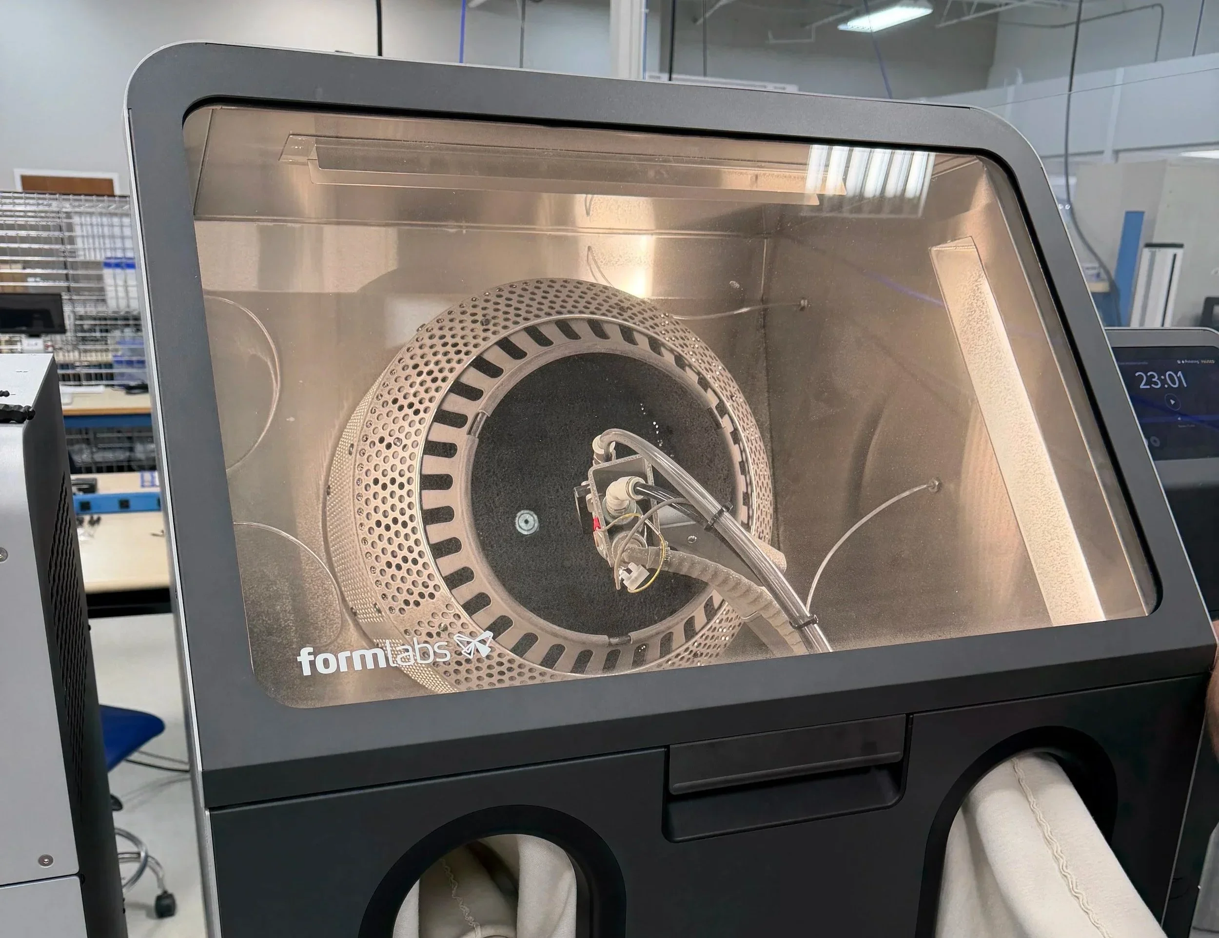 A Formlabs 3D printer with a perforated printing chamber and mechanical components visible through the access window in a laboratory or office setting.