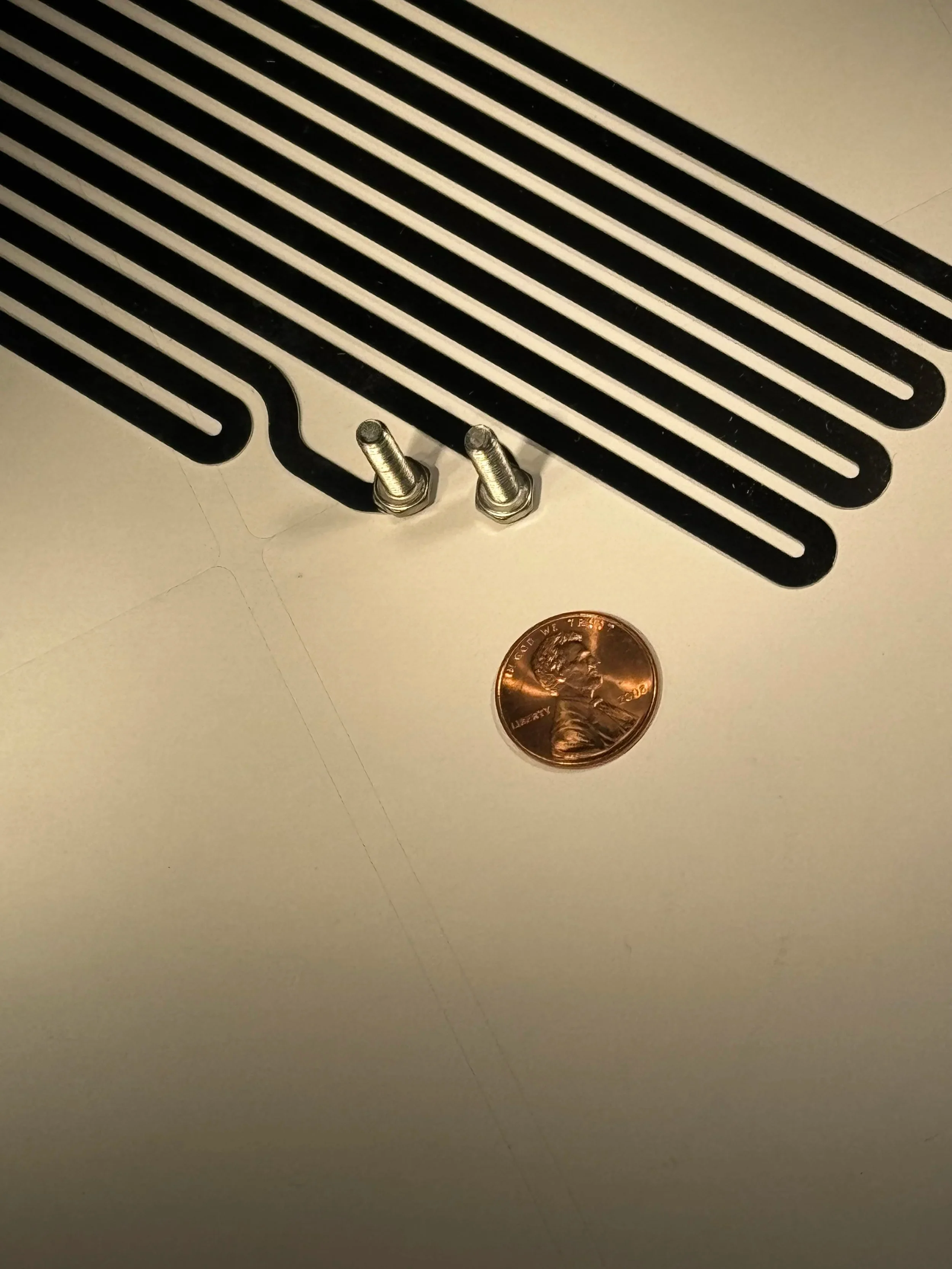 Heating element components with mounting bolts displayed next to a penny for scale on a white surface.