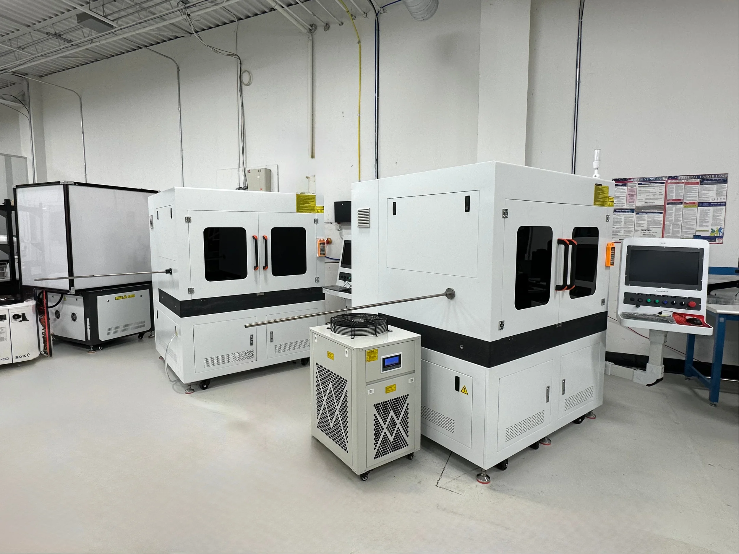 Industrial laser cutting and engraving machines in a manufacturing facility showroom with white walls and concrete flooring.