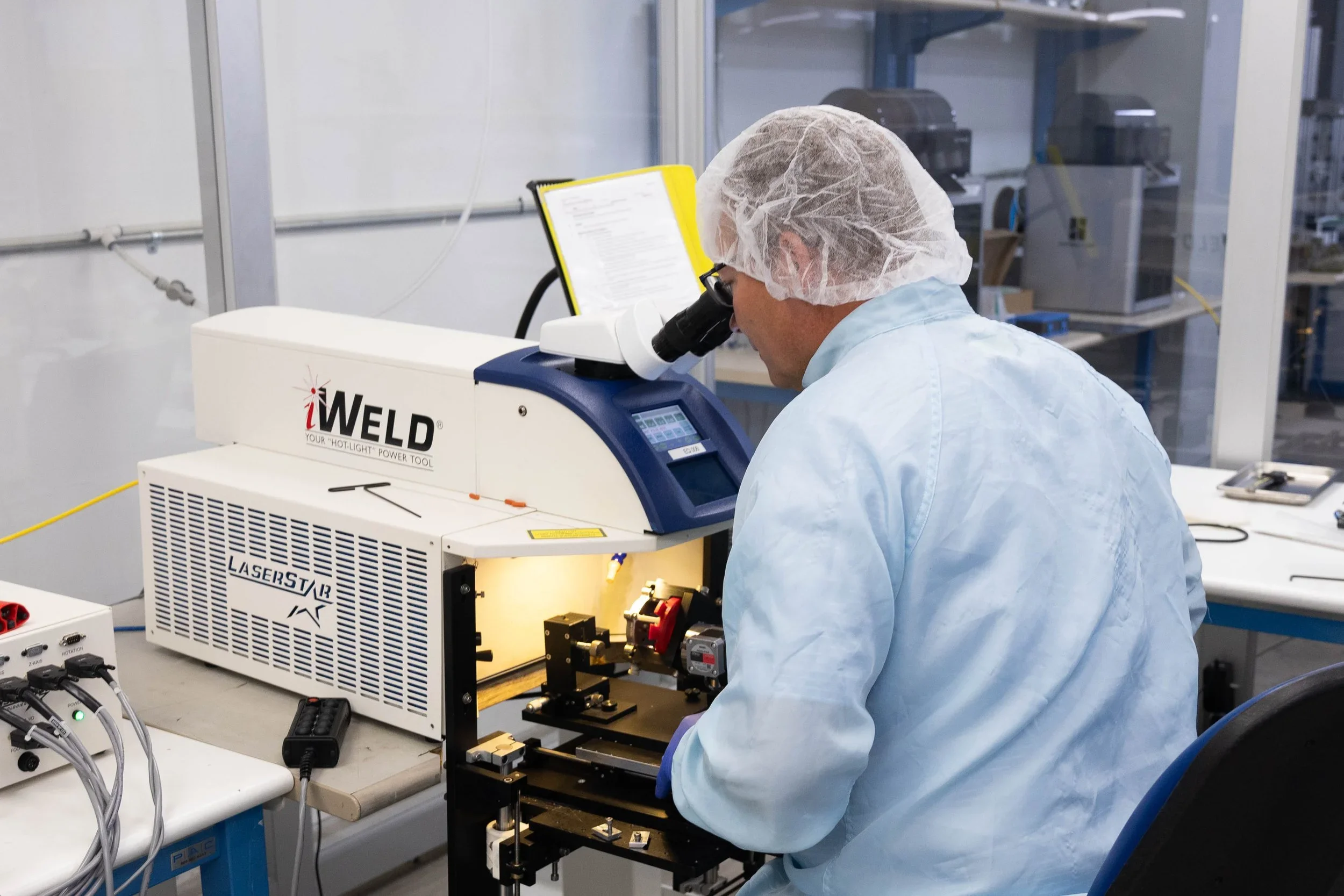 iWELD laser marking and welding equipment being inspected by a technician in a cleanroom laboratory setting.