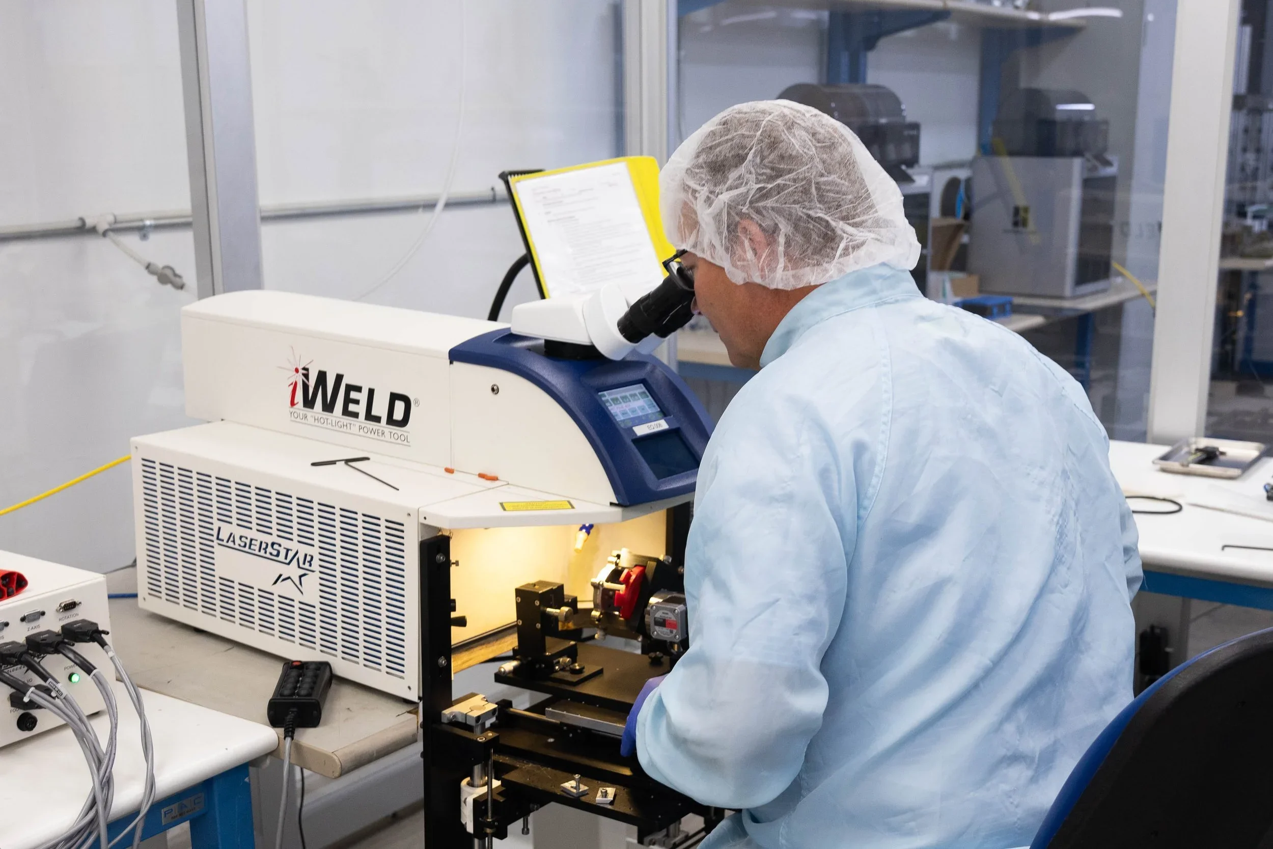 iWELD laser welding system being operated by a technician in a cleanroom laboratory setting.