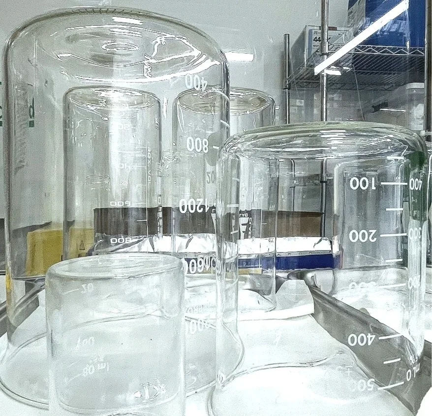 Laboratory beakers and measuring cylinders with liquid samples in a scientific research or testing facility.