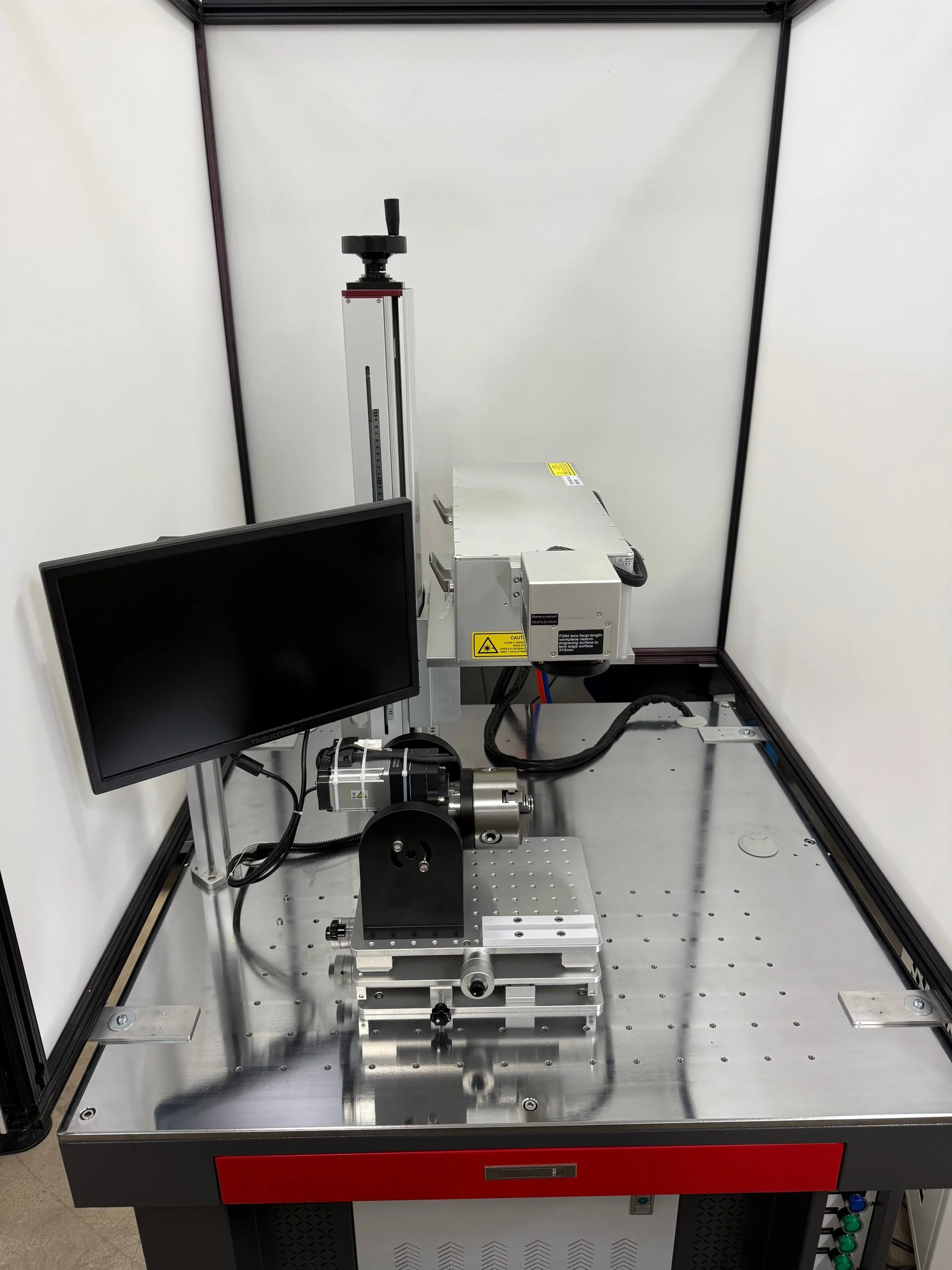 A laser engraving and marking system with control panel and monitor displayed in an enclosed industrial workstation.