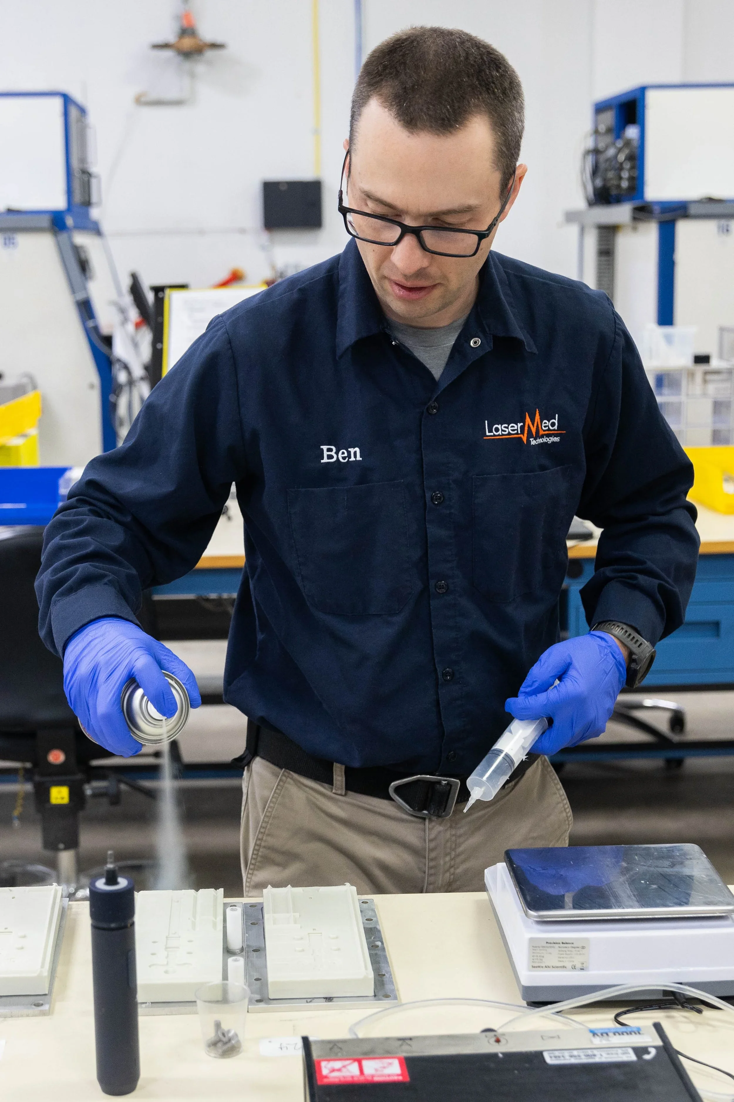 Laser Med technician assembling or inspecting optical and mechanical components in a precision manufacturing workshop setting.