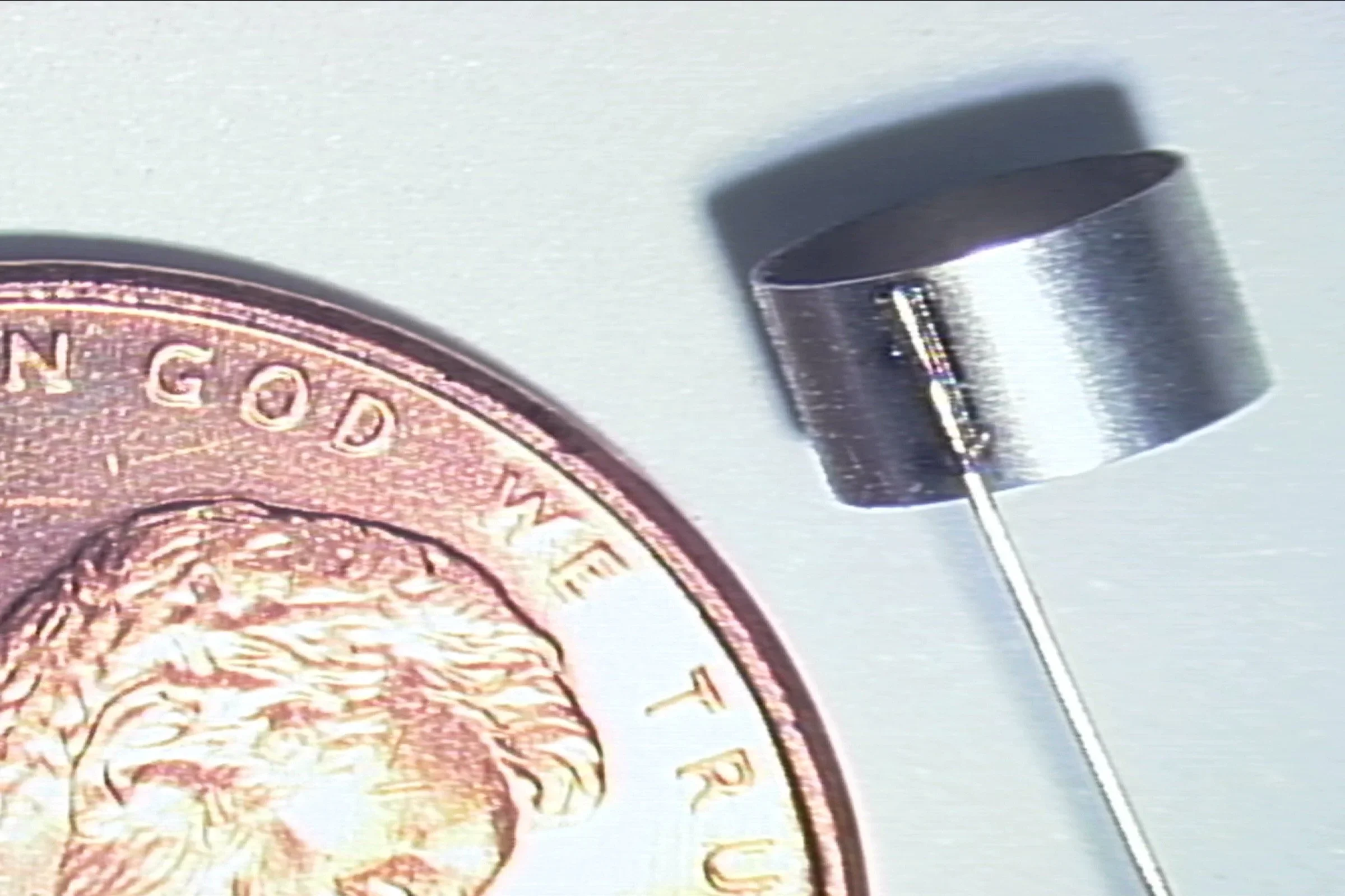 A magnet attachment system being held near a British pound coin to demonstrate magnetic strength and product durability.